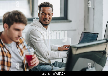 selective focus of angry african american programmer sitting near thoughtful colleague Stock Photo
