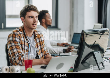 thougtful programmer looking up while working near african american colleague Stock Photo