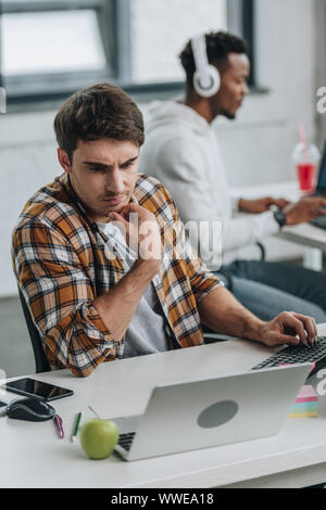 selective focus of thoughtful programmer working near african american colleague in office Stock Photo