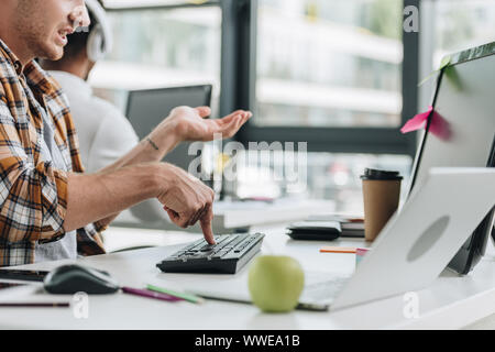 cropped view of programmer gesturing while working in office near african american colleague Stock Photo