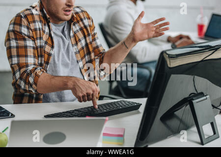 cropped view of programmer gesturing while using computer near african american colleague Stock Photo