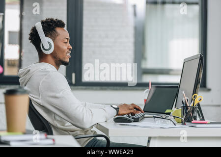 smiling african american programmer in headphones sitting at workplace in office Stock Photo