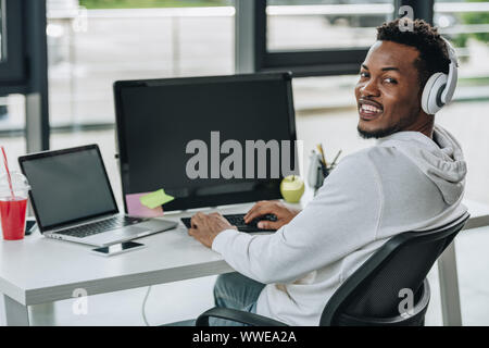 cheerful african american programmer looking at camera while sitting at workplace Stock Photo
