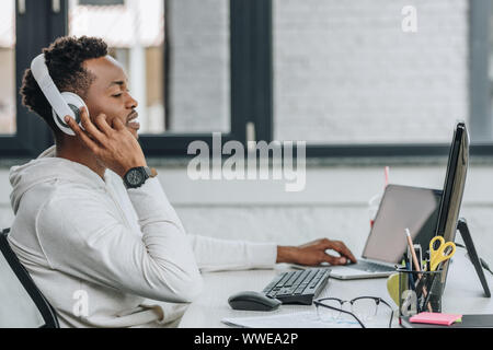 young african american programmer in headphones working on computer in office Stock Photo