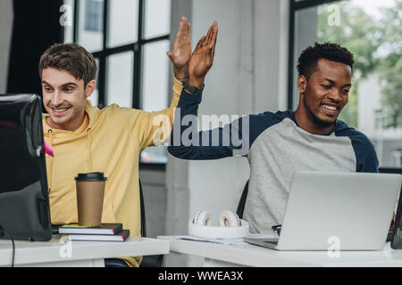 happy multicultural programmers giving high five while working in office together Stock Photo