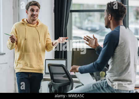 two young multicultural programmers gesturing during discussion in office Stock Photo