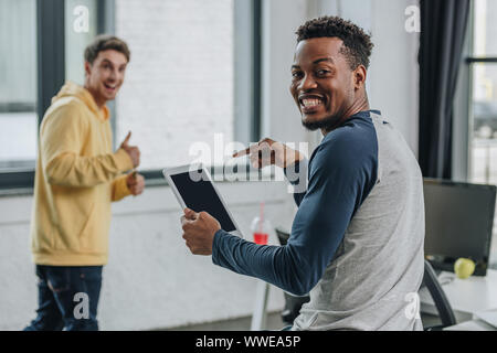 smiling african american programmer pointing with finger at digital tablet near colleague showing thumb up Stock Photo
