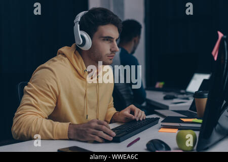selective focus of programmer in headphones working near african american colleague at night in office Stock Photo