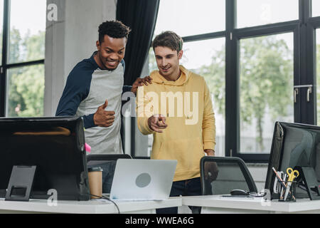 two cheerful multicultural programmers looking at laptop in office Stock Photo