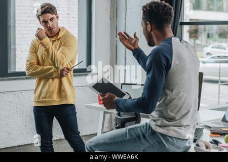 back view of african american programmer gesturing while talking to colleague and holding digital tablet Stock Photo