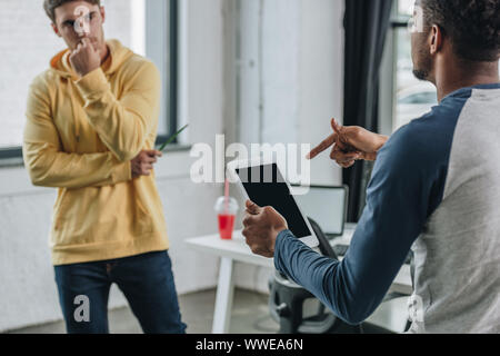 thoughtful programmer looking at african american colleague pointing with finger at digital tablet Stock Photo