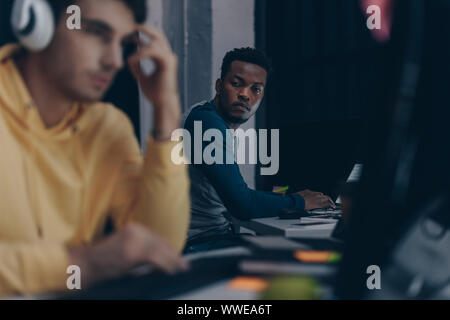 selective focus of african american programmer looking at colleague in headphones Stock Photo