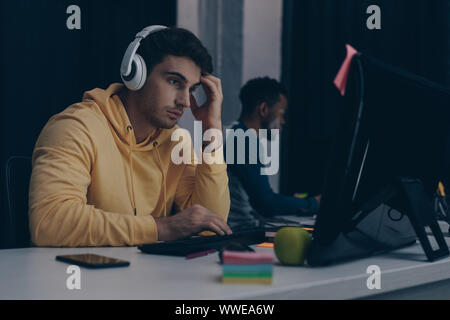 selective focus of thoughtful programmer in headphones working near african american colleague Stock Photo