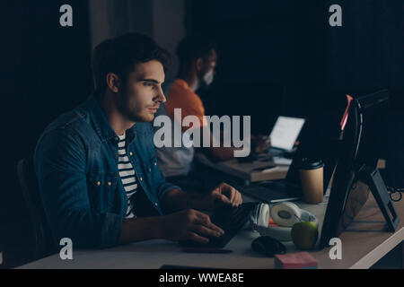 selective focus of young programmer working at night near african american colleague Stock Photo