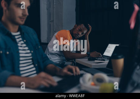 selective focus of african american programmer looking at multicultural colleague while working together at night in office Stock Photo