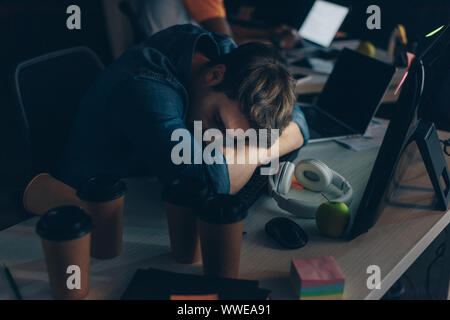 young, exhausted programmer sleeping at workplace at night in office Stock Photo