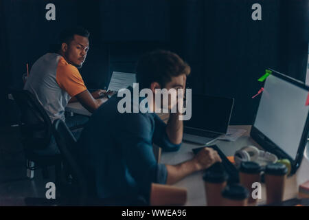 selective focus of african american programmer looking at multicultural colleague while working at night in office Stock Photo