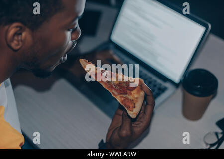 young african american programmer eating pizza while working at night in office Stock Photo