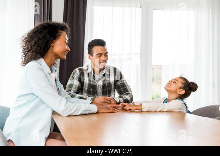 african american family sitting before table, smiling and looking at each other Stock Photo