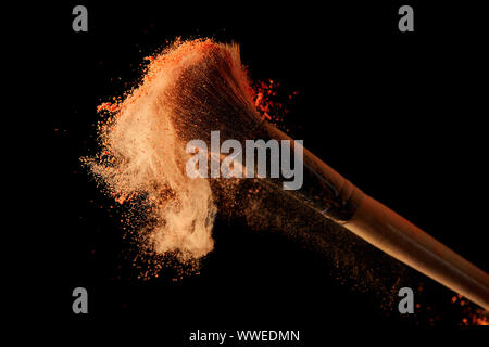 cosmetic brush with orange powder explosion on black background Stock Photo