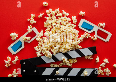 top view of delicious popcorn near clapper board and 3d glasses on red background Stock Photo