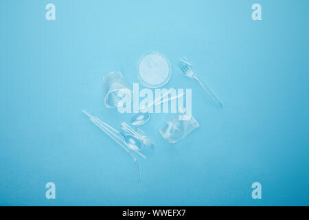 top view of pile of transparent disposable cups, forks and spoons on blue background Stock Photo