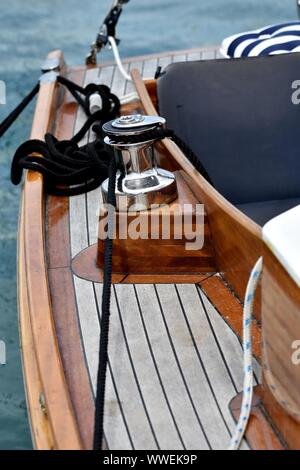 Wooden sailboat moored at the marina. Details of a classic sailing yacht with teak deck, varnished wood, winch and ropes on blurred background Stock Photo