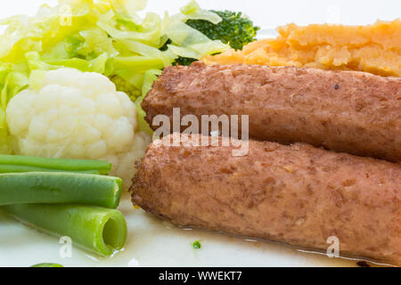 Meat free vegetarian and vegan sausages. On a plate with vegetables - french beans, cauliflower, cabbage, broccoli and sweet potato mash. Stock Photo