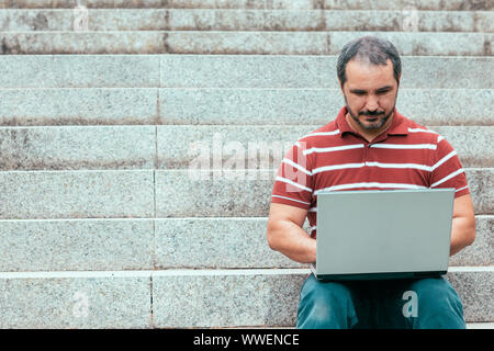 man sitting on staircase outside and working on laptop. Stock Photo