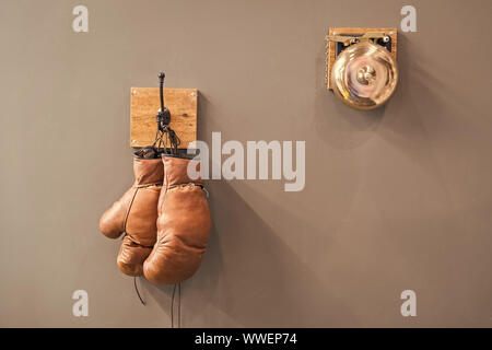 Final sparring. Vintage boxing gloves hang on hook wall background. Boxing gloves and ring bell. Boxing career famous sportsman. Museum of box sport. Box exhibition retro attributes. Boxing school. Stock Photo