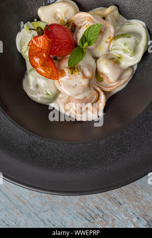 different types of pelmeni in black plate on wooden background Stock Photo