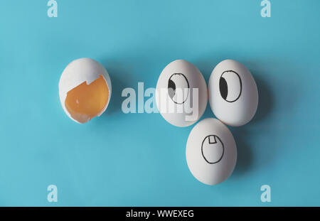 White eggs with faces painted in the shell next to a broken egg Stock Photo