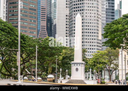 Singapore - March 20, 2019: White tall Dalhousie Obelisk on pedestal in front of skyscrapers of Financial District. Some green foliage at the fringes, Stock Photo