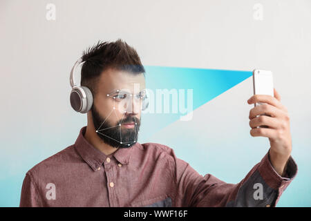 Young man with headphones and mobile phone using facial recognition system for data protection Stock Photo