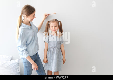 Young mother measuring height of her little daughter near light wall Stock Photo