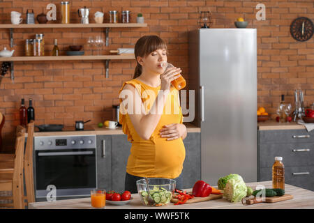 Young pregnant woman drinking juice in kitchen Stock Photo