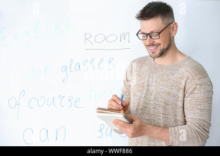 Handsome male teacher writing in notebook near blackboard in classroom Stock Photo