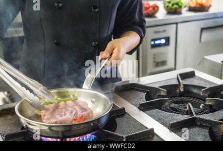 Close-up of a meal being prepared on an industrial gas stove by a female professional chef in a restaurant kitchen in the Philippines. No face visible. Stock Photo