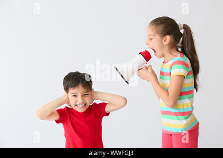 Little girl with megaphone screaming on boy against light background Stock Photo