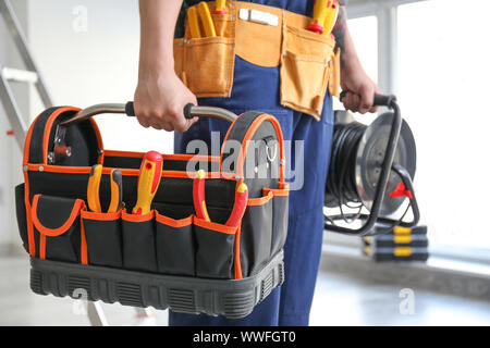 Electrician with tools and cable extender indoors Stock Photo