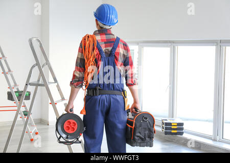 Electrician with tools and cable extender indoors Stock Photo