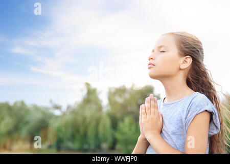 Little girl praying to God outdoors Stock Photo