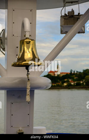 Bronze bell on the deck of a ship. In the background you can see Wallsee Castle in Wallsee-Sindelburg. Austria Stock Photo