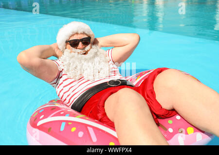 Santa Claus relaxing on inflatable ring in swimming pool Stock Photo