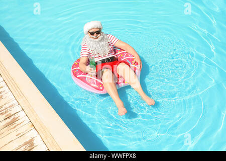 Santa Claus relaxing on inflatable ring in swimming pool Stock Photo