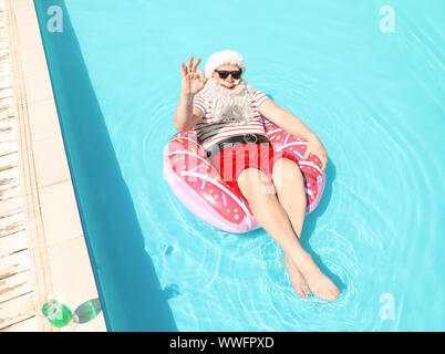 Santa Claus relaxing on inflatable ring in swimming pool Stock Photo