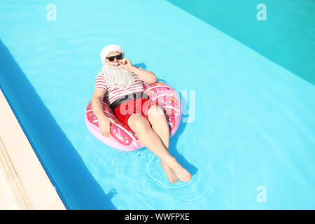 Santa Claus relaxing on inflatable ring in swimming pool Stock Photo