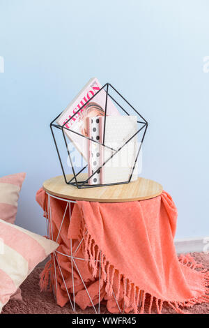 Stylish holder with books and magazine on table in room Stock Photo