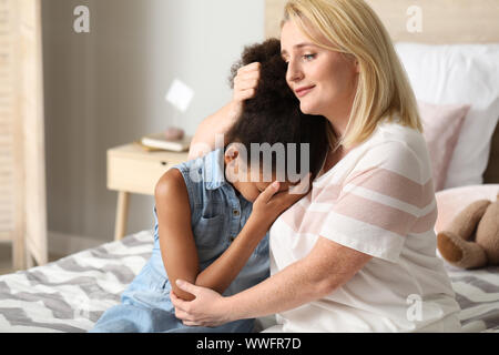 Woman calming her crying African-American daughter at home Stock Photo