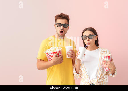 Emotional couple with popcorn and drink watching movie on color background Stock Photo
